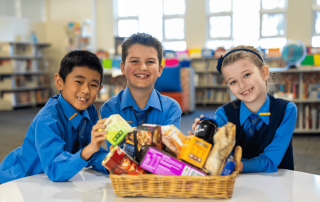 Three students smile at the camera as they show off a lovely Christmas hamper they have made